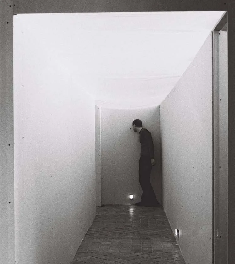 fragment instalacji Leaving Room - korytarz wejściowy prowadzący do wystawy: ściany z płyty kartonowo-gipsowej, lampki gniazdkowe, notesy i 